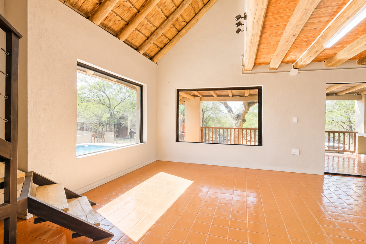 Spacious living area featuring high vaulted ceilings with exposed timber rafters, terracotta tiled flooring, and large windows providing natural light and outdoor views.