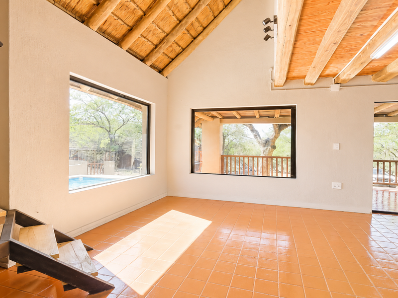 Spacious living area featuring high vaulted ceilings with exposed timber rafters, terracotta tiled flooring, and large windows providing natural light and outdoor views.