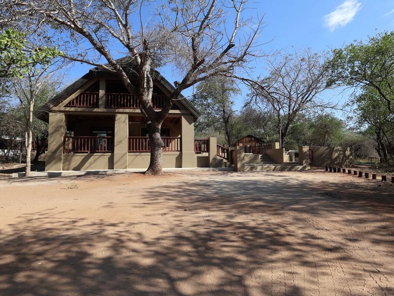 Front view of a well-maintained thatched-roof house featuring a covered patio, timber balcony railings, and a spacious natural landscape setting.