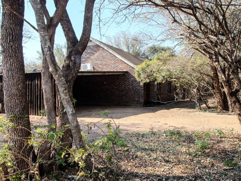 A view of the front exterior of a face brick house featuring a covered carport and natural wooded surroundings.