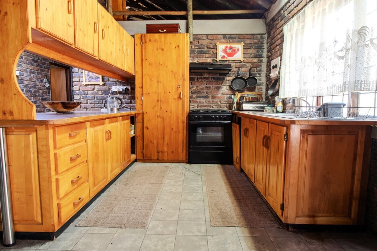 Rustic kitchen featuring exposed brick walls, timber cabinetry, built-in oven, and exposed ceiling beams, offering a warm, traditional aesthetic with functional layout.