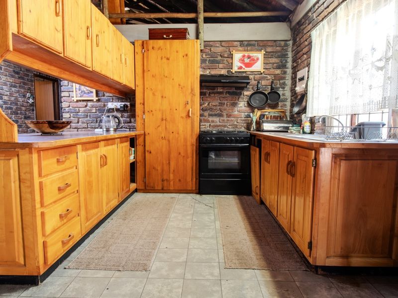 Rustic kitchen featuring exposed brick walls, timber cabinetry, built-in oven, and exposed ceiling beams, offering a warm, traditional aesthetic with functional layout.