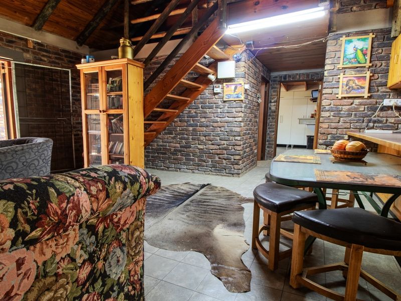Open-plan living and dining area featuring exposed brick walls, timber staircase, and rustic wooden ceiling beams with integrated kitchen cabinetry.