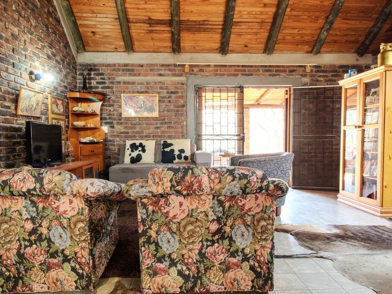Rustic living room featuring exposed brick walls, a high timber beam ceiling, and tiled flooring with direct access to an outdoor area.