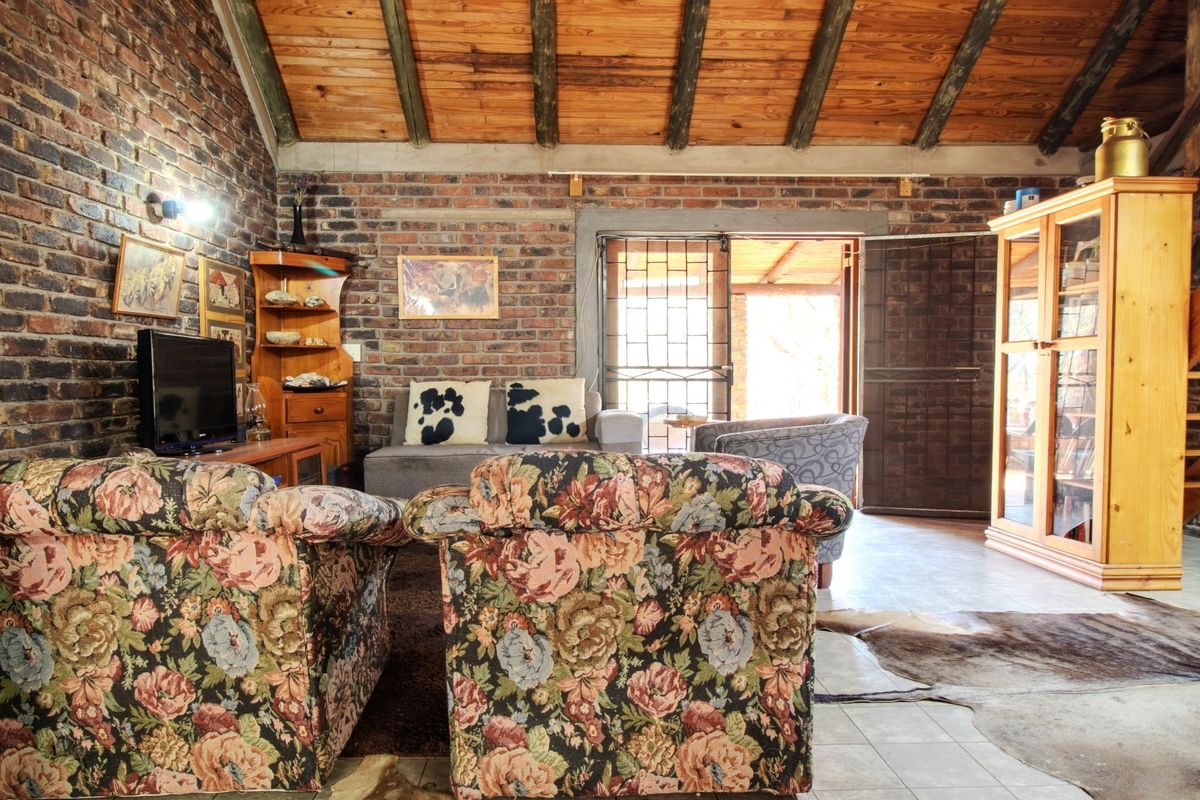 Rustic living room featuring exposed brick walls, a high timber beam ceiling, and tiled flooring with direct access to an outdoor area.