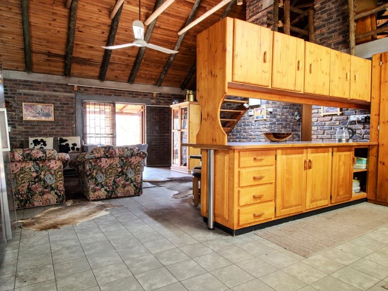 Open-plan living and kitchen area featuring exposed brick walls, timber beam ceilings, and wooden cabinetry with tiled flooring throughout.