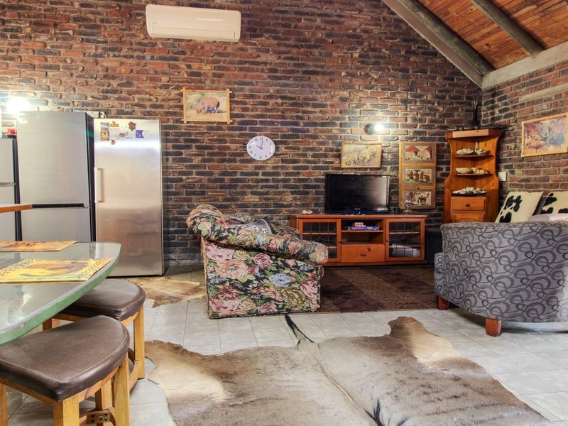 Open-plan living area featuring exposed brick walls, high timber-beamed ceilings, and tiled flooring, creating a rustic and spacious atmosphere.