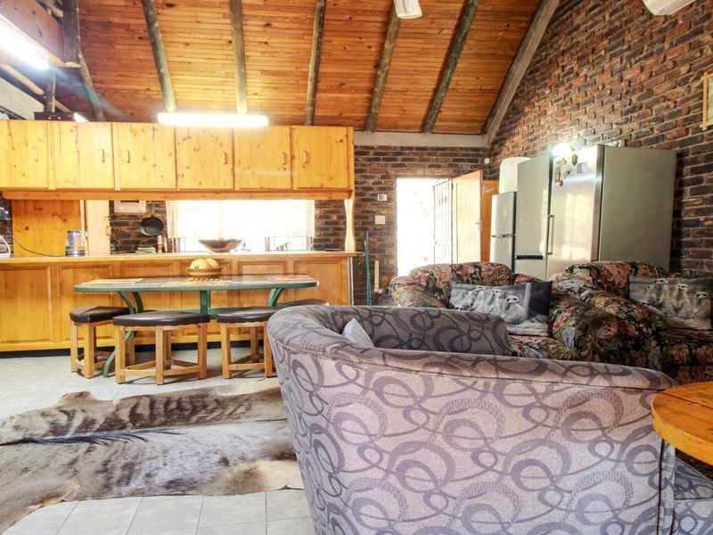 Open plan living and kitchen area featuring exposed brick walls, high timber beam ceilings, and traditional wooden cabinetry.