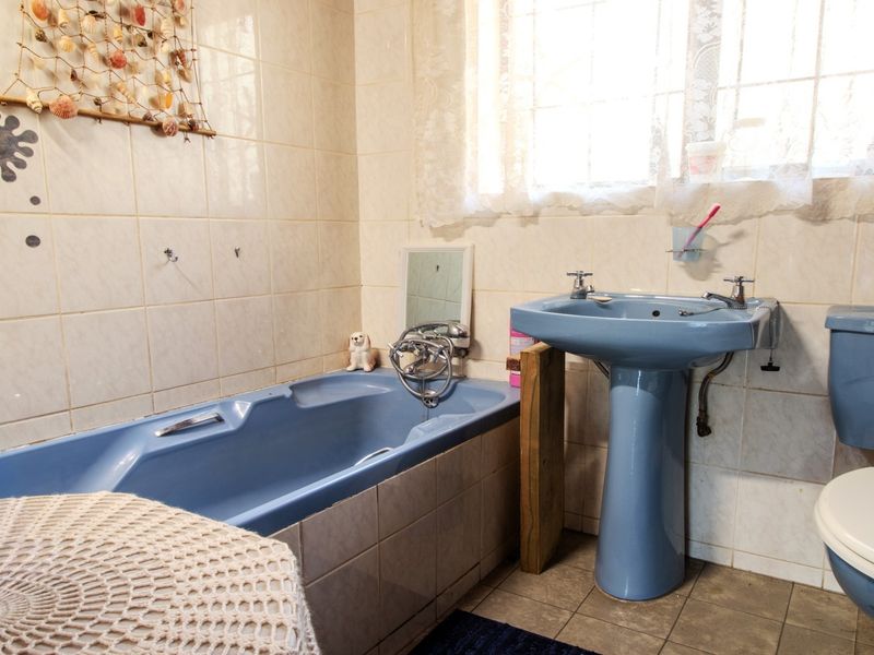 A dated bathroom featuring a blue pedestal basin, matching bathtub, and toilet, with tiled walls and flooring, offering potential for modern renovation.