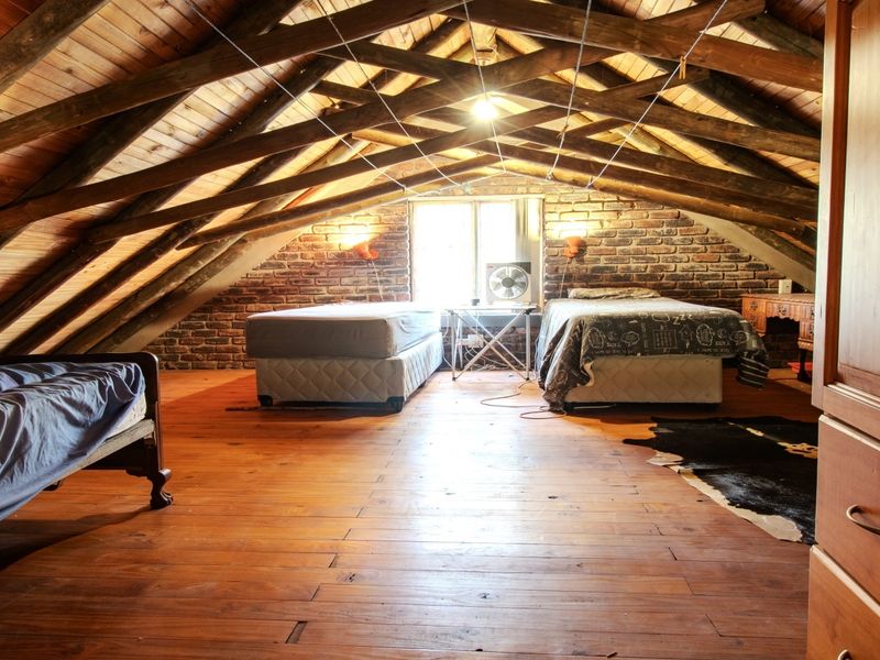 Spacious attic bedroom featuring exposed timber roof trusses, warm timber flooring, and rustic exposed brick walls.