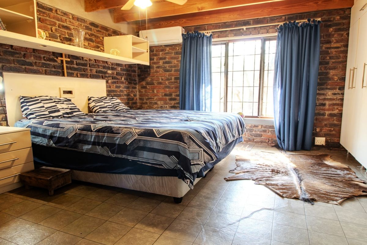 A bedroom featuring exposed brick walls, timber ceiling beams, tiled flooring, and built-in storage, offering a rustic aesthetic with modern climate control.
