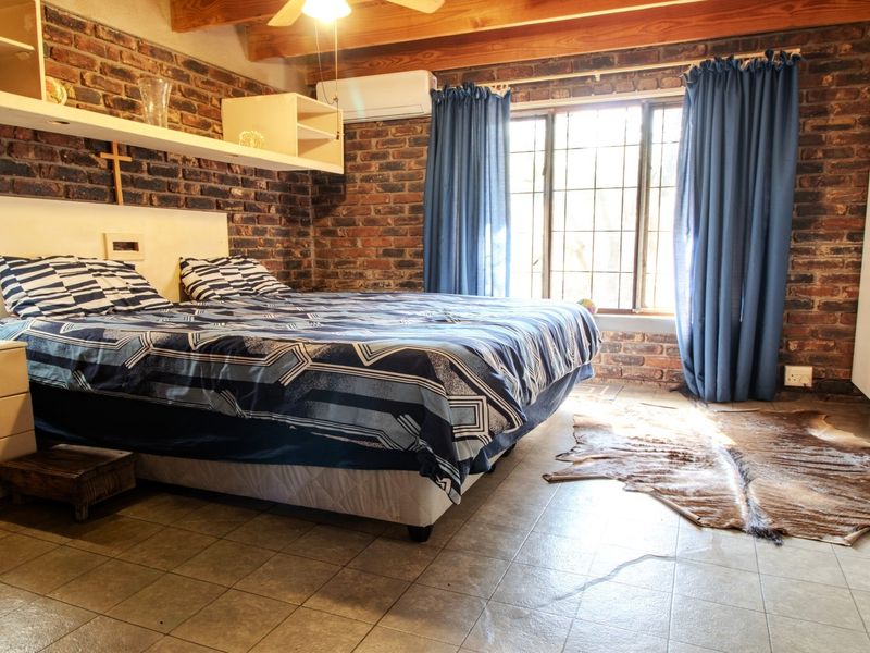 A bedroom featuring exposed brick walls, timber ceiling beams, tiled flooring, and built-in storage, offering a rustic aesthetic with modern climate control.