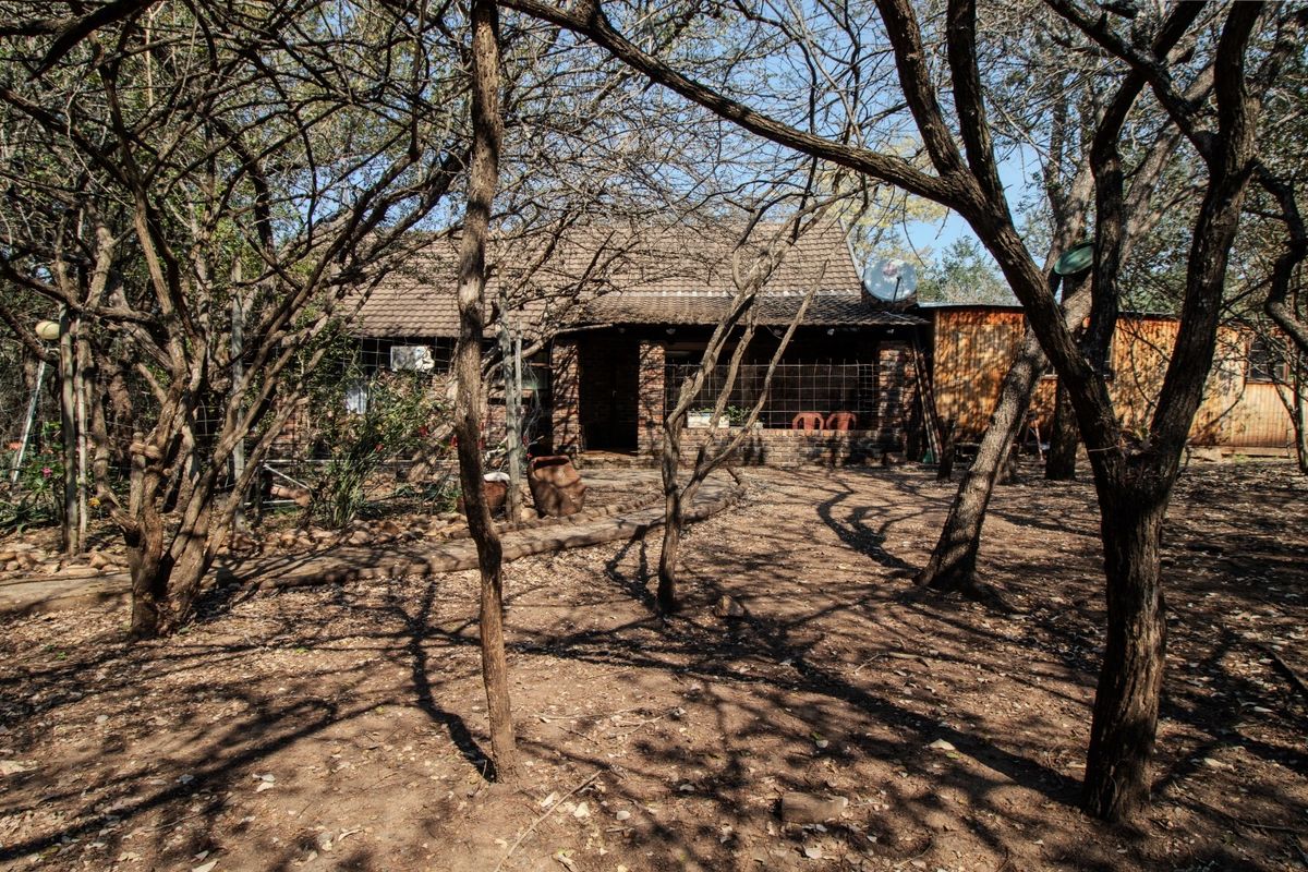 Rear view of a brick house featuring a covered patio area, set within a wooded garden plot.