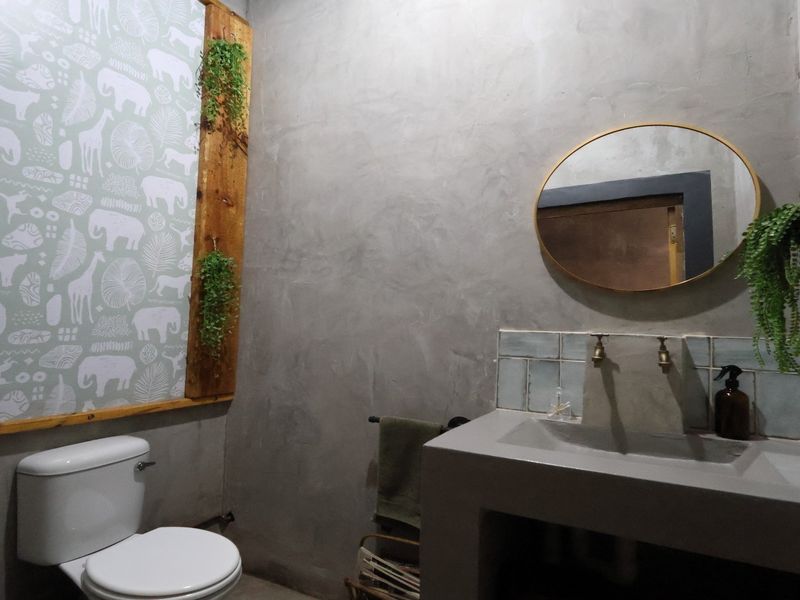 A modern bathroom featuring a custom cement vanity with brass taps, a tiled splashback, and a minimalist cement plaster wall finish.
