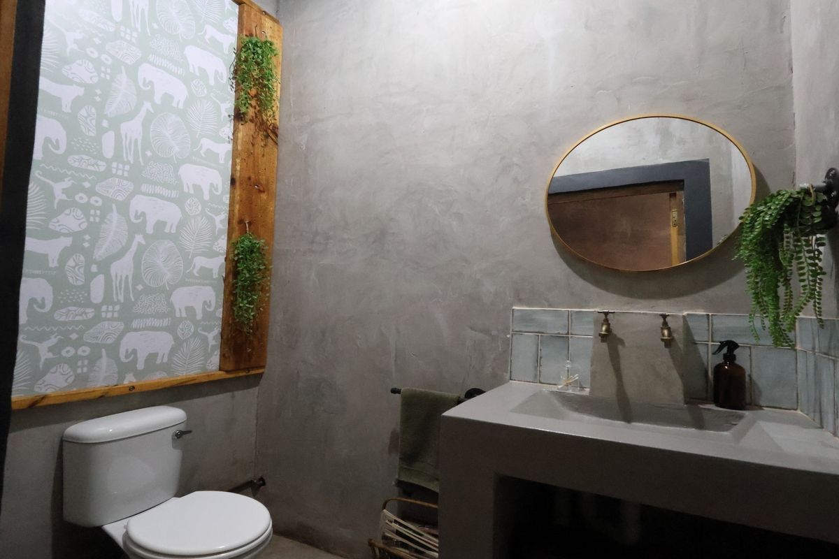 A modern bathroom featuring a custom cement vanity with brass taps, a tiled splashback, and a minimalist cement plaster wall finish.