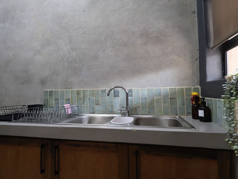 A functional scullery area featuring a double bowl stainless steel sink, concrete countertop, and wooden cabinetry with a decorative tiled splashback.