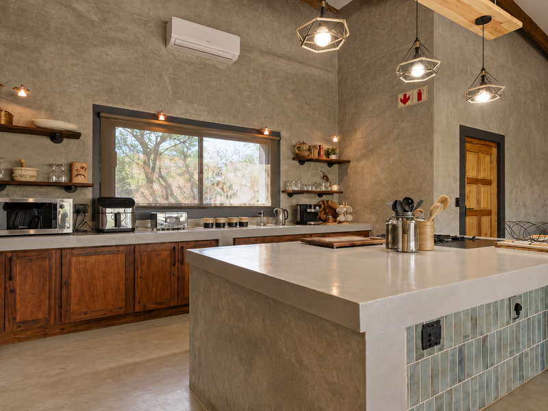 Modern industrial-style kitchen featuring a large concrete island, custom wooden cabinetry, exposed brick accents, and high-quality pendant lighting.