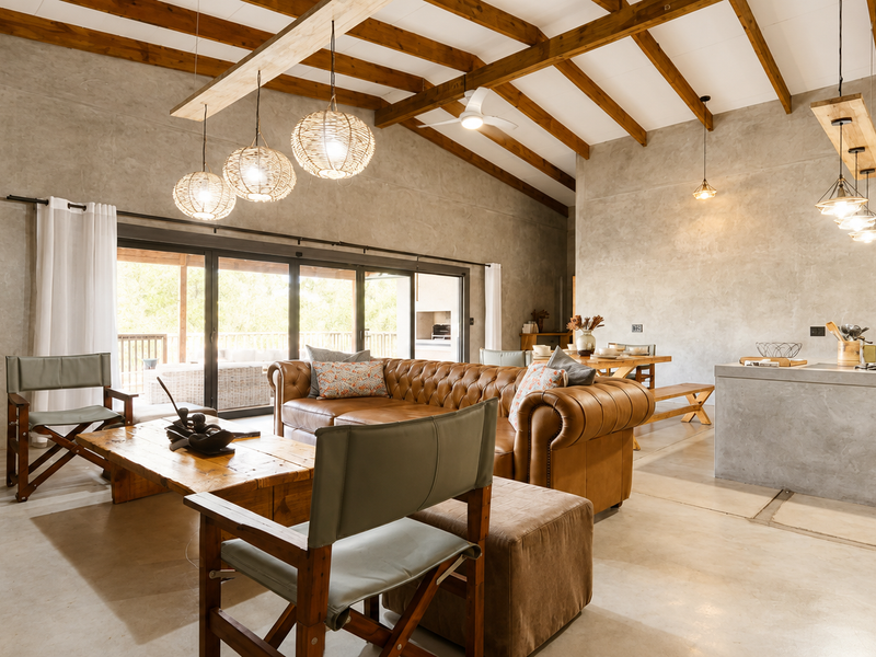 Spacious open-plan living and kitchen area featuring polished concrete floors, exposed timber beams, vaulted ceilings, and large sliding doors leading to the patio.