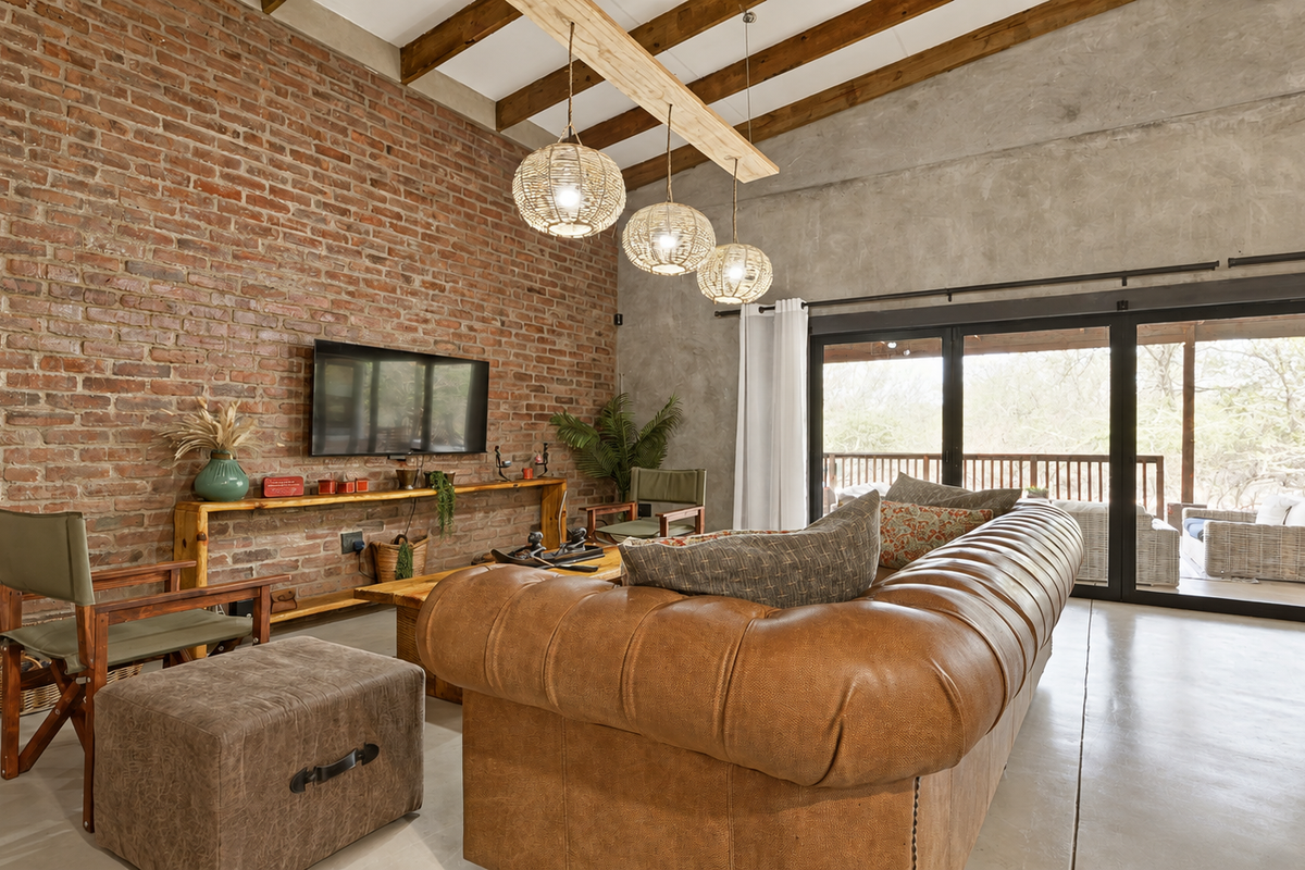 Spacious living room featuring exposed brick and concrete walls, high timber-beamed ceilings, polished concrete floors, and large bi-fold doors opening to the outdoors.