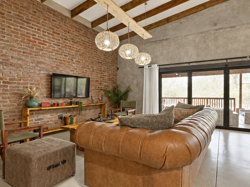 Spacious living room featuring exposed brick and concrete walls, high timber-beamed ceilings, polished concrete floors, and large bi-fold doors opening to the outdoors.