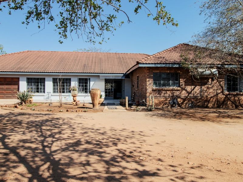 Front elevation of a single-story brick house featuring a tiled roof, integrated garage, and steel-framed windows, set on a large open plot.