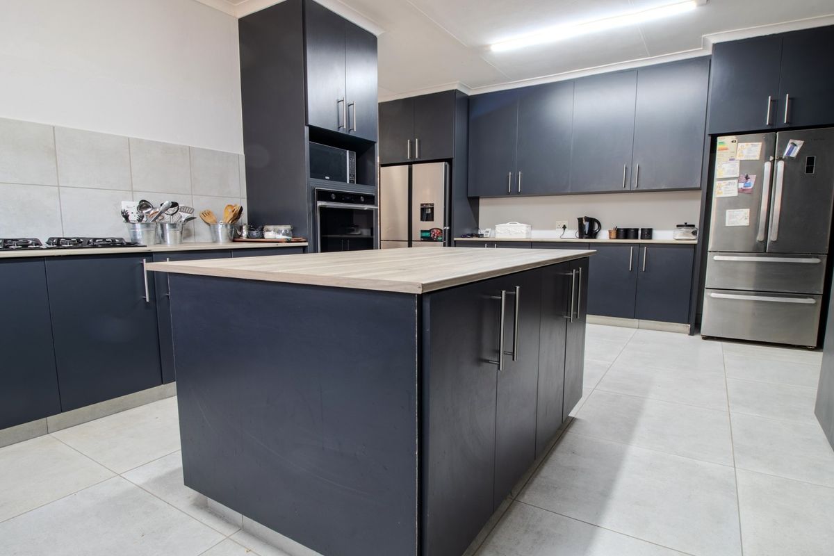 Modern kitchen featuring dark cabinetry, a central island with a wood-look countertop, built-in oven, gas hob, and light-colored tiled flooring.