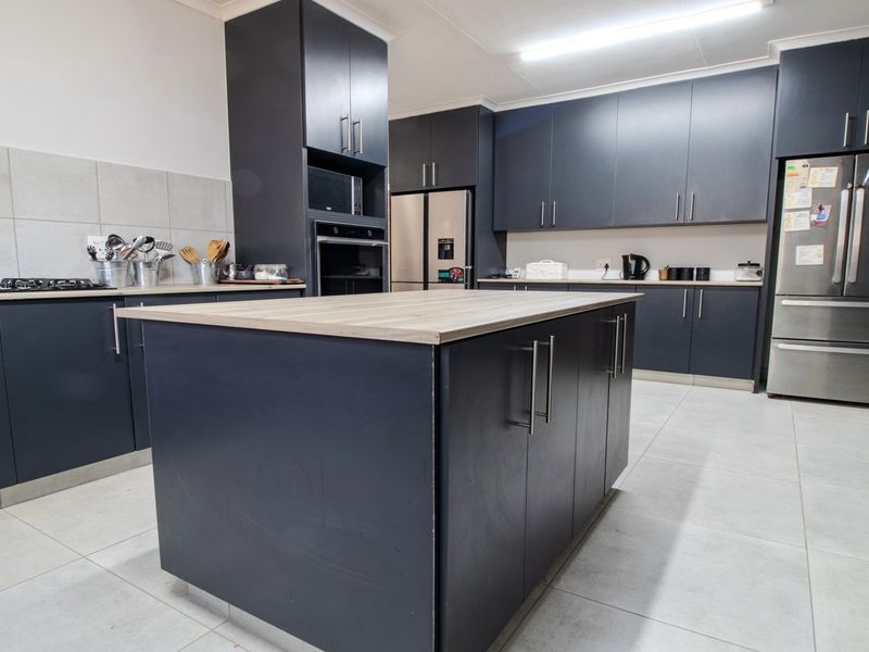 Modern kitchen featuring dark cabinetry, a central island with a wood-look countertop, built-in oven, gas hob, and light-colored tiled flooring.