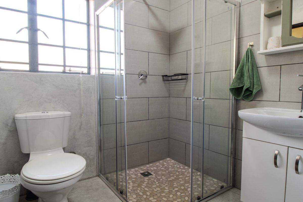 A modern bathroom featuring a glass-enclosed shower with pebble flooring, a vanity basin, and a toilet, complemented by neutral wall tiling.