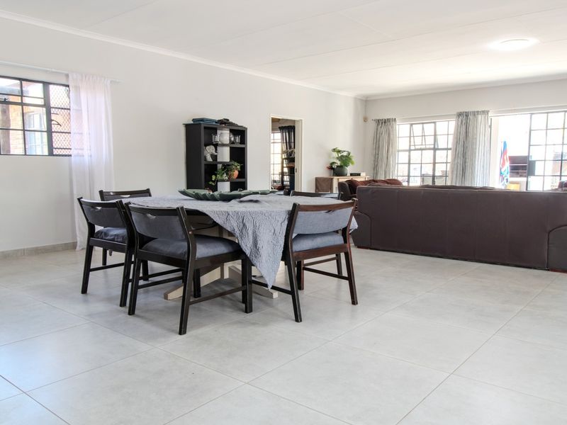 Spacious open-plan living and dining area featuring neutral tiled flooring and large steel-framed windows providing ample natural light.
