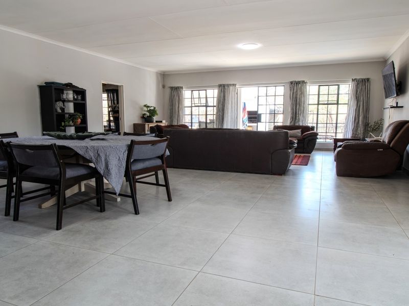 Spacious open-plan living and dining area featuring large steel-framed windows, neutral tiled flooring, and a bright, functional layout.