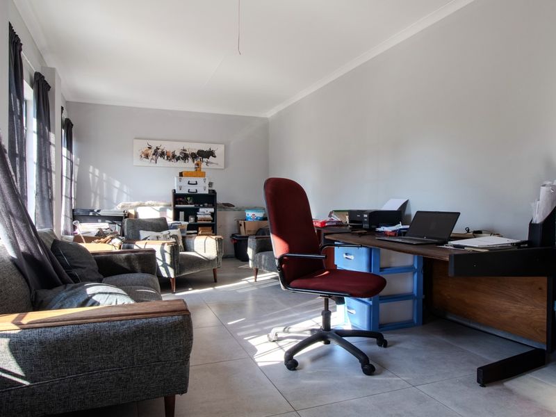 A functional home office space featuring neutral tiled flooring and large windows that provide ample natural light.