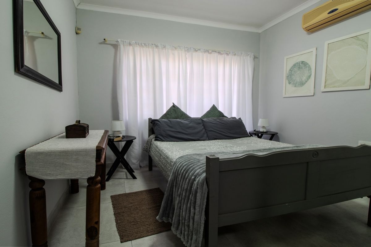 A functional bedroom featuring tiled flooring and a wall-mounted air conditioning unit, providing a comfortable and neutral living space.