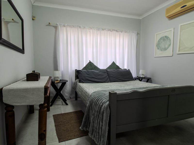 A functional bedroom featuring tiled flooring and a wall-mounted air conditioning unit, providing a comfortable and neutral living space.