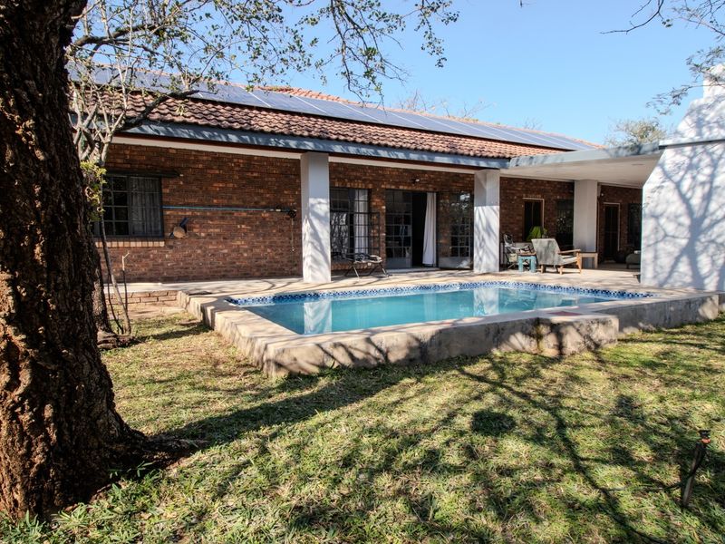 A rear exterior view featuring a swimming pool, covered patio area, brick facade, and solar panels installed on the tiled roof.