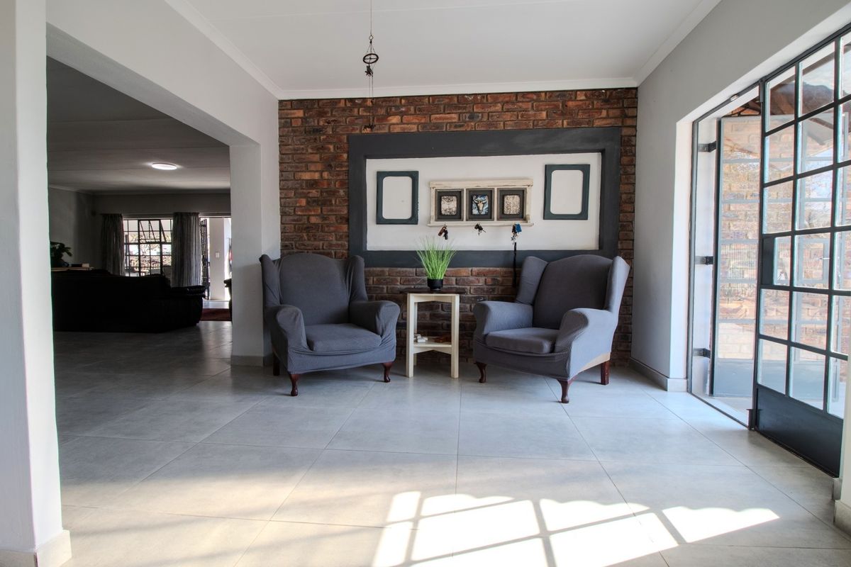 A bright living area featuring a prominent exposed brick feature wall, large format floor tiles, and a steel-framed glass door leading outdoors.