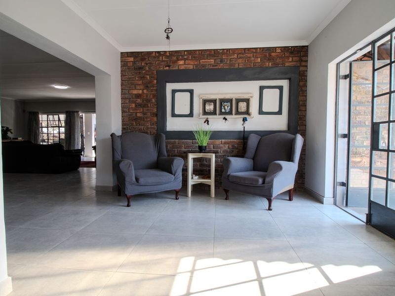 A bright living area featuring a prominent exposed brick feature wall, large format floor tiles, and a steel-framed glass door leading outdoors.