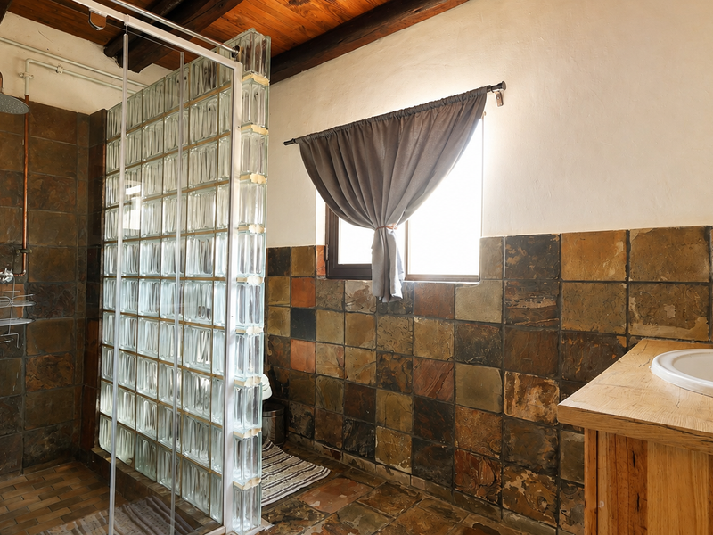 Bathroom featuring rustic slate tiling, exposed timber ceiling beams, a glass block shower partition, and a timber vanity with a basin.