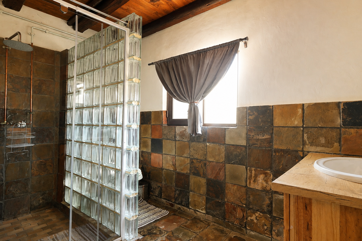 Bathroom featuring rustic slate tiling, exposed timber ceiling beams, a glass block shower partition, and a timber vanity with a basin.