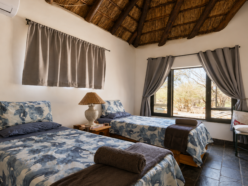 A bedroom featuring a traditional thatched roof with exposed timber rafters, slate tile flooring, and a split-system air conditioner.