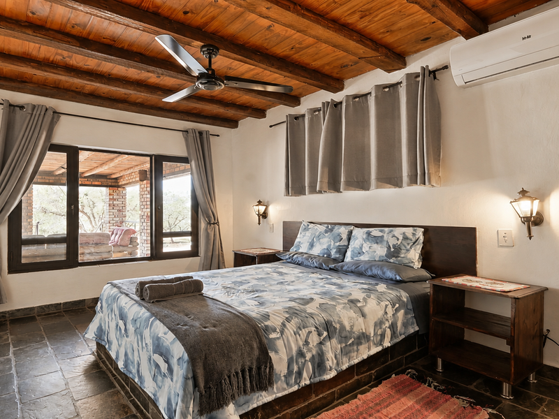 A cozy bedroom featuring exposed timber beam ceilings, stone tile flooring, a split-system air conditioner, and direct access to an outdoor patio area.