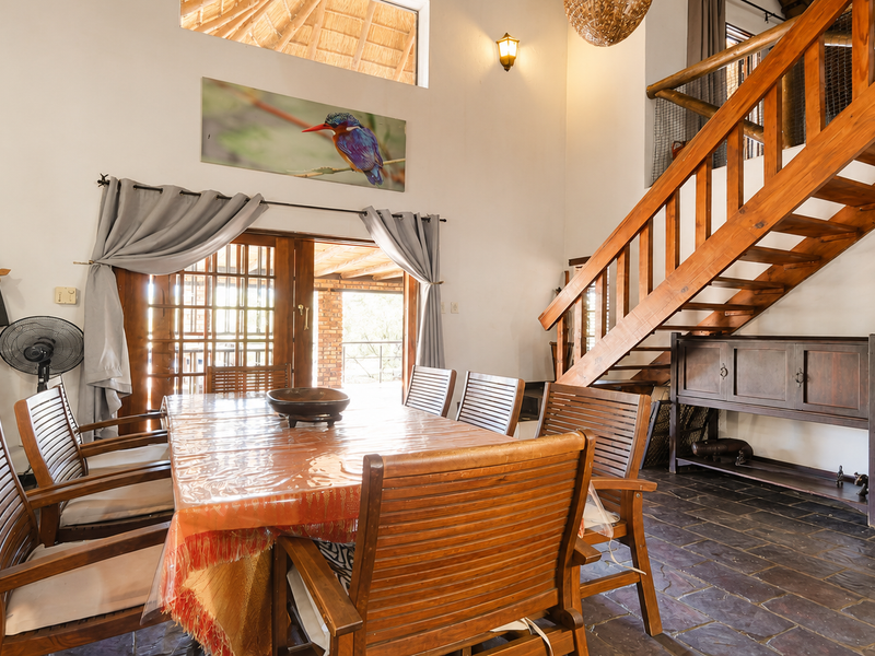 Dining area featuring slate tile flooring, a prominent wooden staircase, and timber-framed sliding doors leading to an outdoor space under a thatched roof.