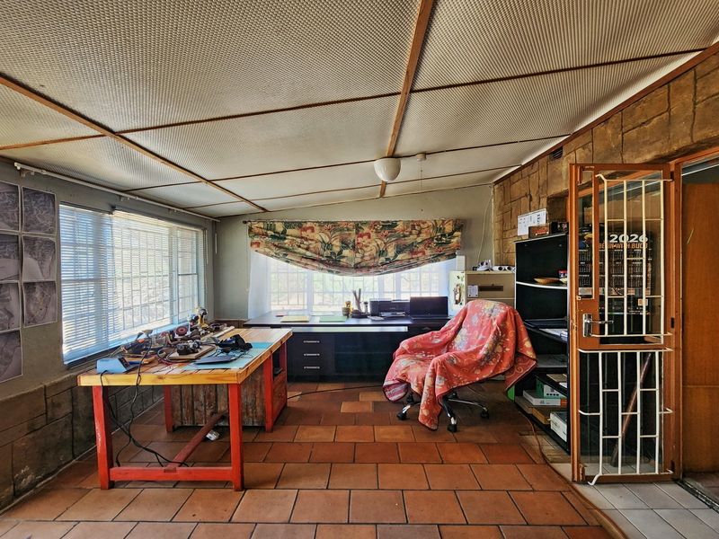 A functional office space featuring terracotta tile flooring, a stone feature wall, and a suspended ceiling, offering potential for a modern workspace conversion.
