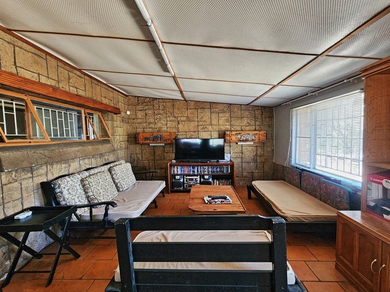 A living room featuring stone-clad walls, terracotta floor tiles, and a suspended ceiling, offering a dated aesthetic with potential for modernization.