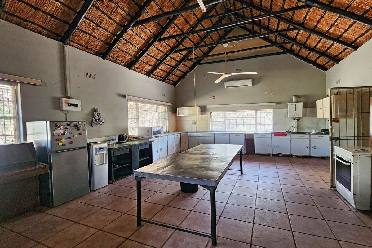 Spacious kitchen featuring a high thatched roof with exposed trusses, tiled flooring, and extensive built-in cabinetry with a central prep island.