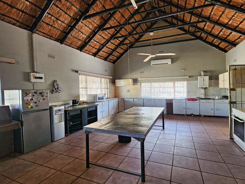 Spacious kitchen featuring a high thatched roof with exposed trusses, tiled flooring, and extensive built-in cabinetry with a central prep island.