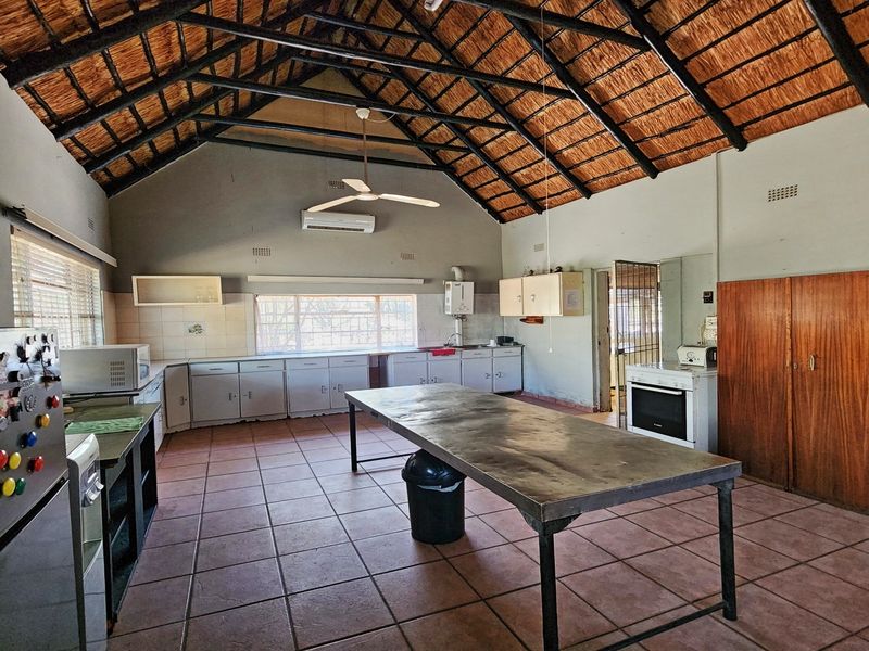 Spacious kitchen featuring a high thatched ceiling with exposed trusses, tiled flooring, extensive built-in cabinetry, and an air conditioning unit.