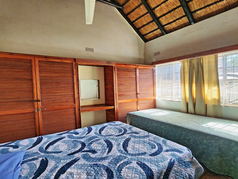 Bedroom featuring a vaulted thatched ceiling, tiled flooring, and extensive built-in wooden cabinetry with an integrated vanity area.