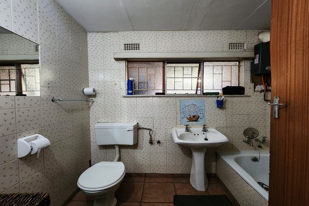 A functional bathroom featuring a pedestal basin, toilet, and bathtub with dated wall tiling and original fixtures, offering potential for modernization.