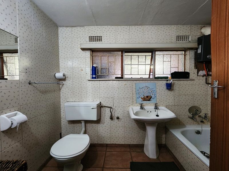 A functional bathroom featuring a pedestal basin, toilet, and bathtub with dated wall tiling and original fixtures, offering potential for modernization.