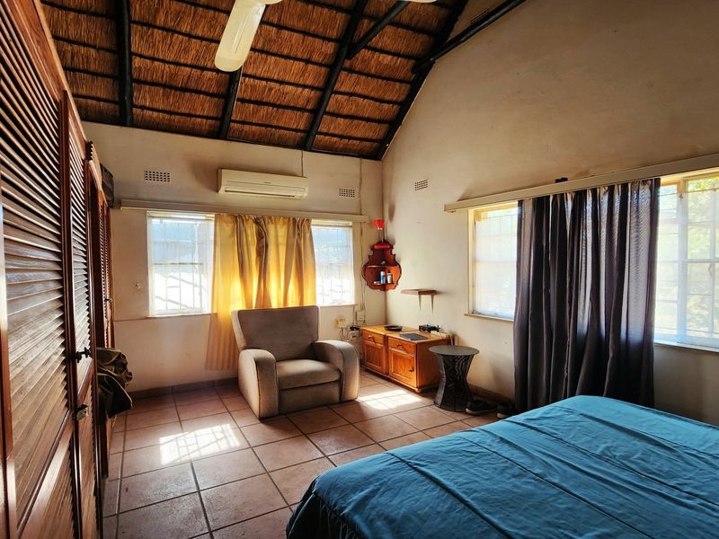 Spacious bedroom featuring a high vaulted thatch ceiling with exposed rafters, tiled flooring, built-in wooden cupboards, and a wall-mounted air conditioning unit.
